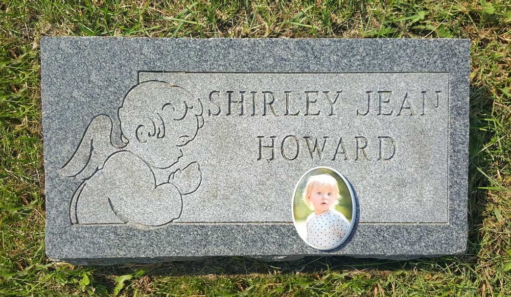 A child's headstone with a small oval ceramic memorial photo, provided through the Gone Too Soon Program